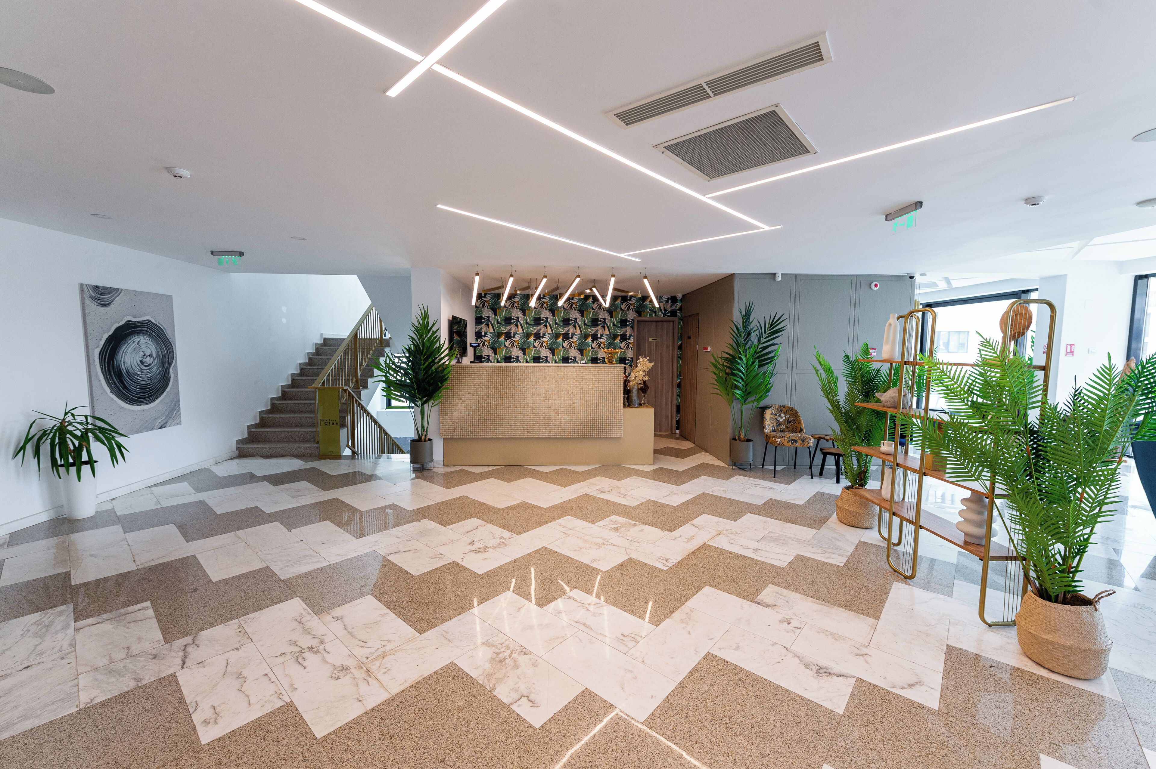 A modern lobby with a herringbone patterned floor, a reception desk, and potted plants.
