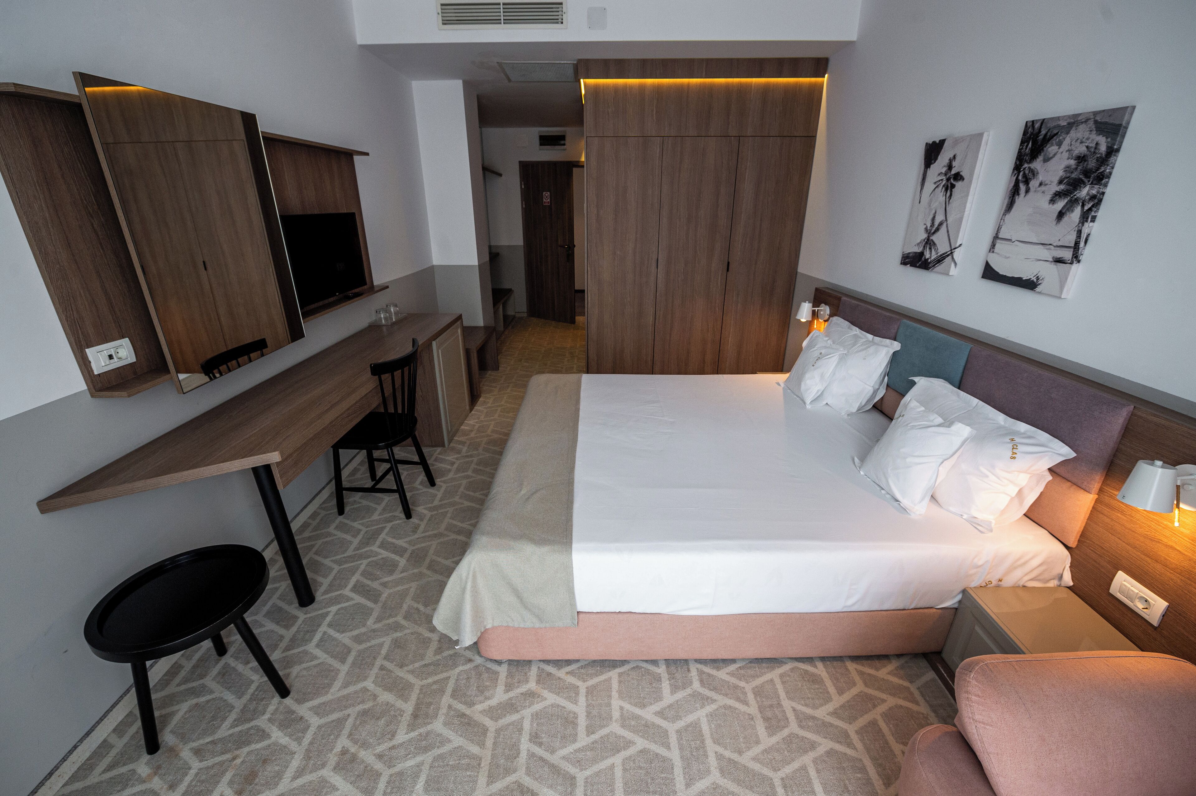 A hotel room with a bed, bedside table, lamp, and a desk with a chair.