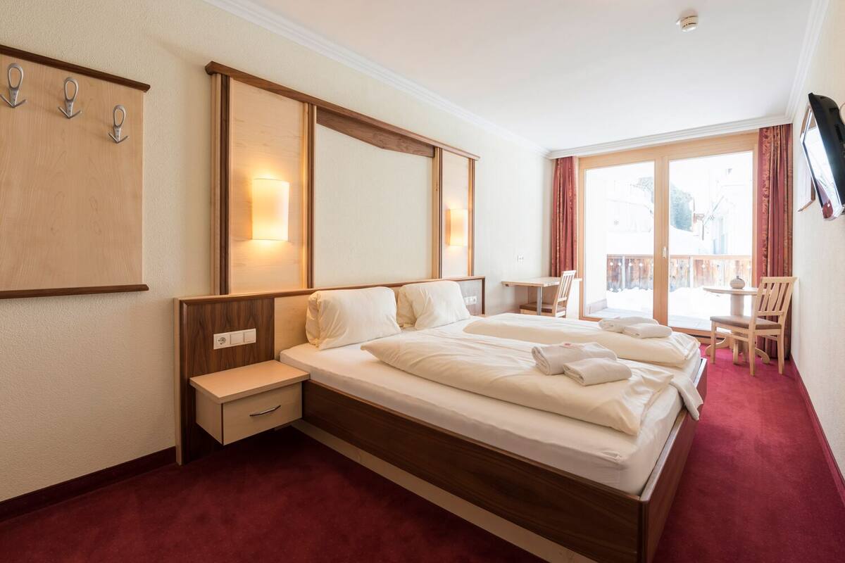 A hotel room with a large bed, a desk, and a chair near a window.
