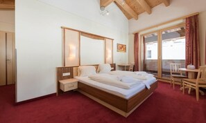 A bedroom with a large bed, a bedside table, a chair, and a view of the outside through a sliding glass door. - Hotel Abendrot by Alpeffect Hotels (Ischgl)