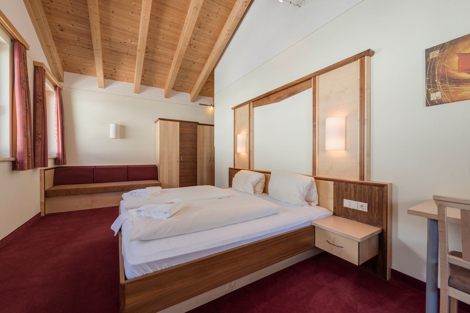 Ein Schlafzimmer mit einem hölzernen Bett, einem Nachttisch, einer Bank und einem Kleiderschrank.