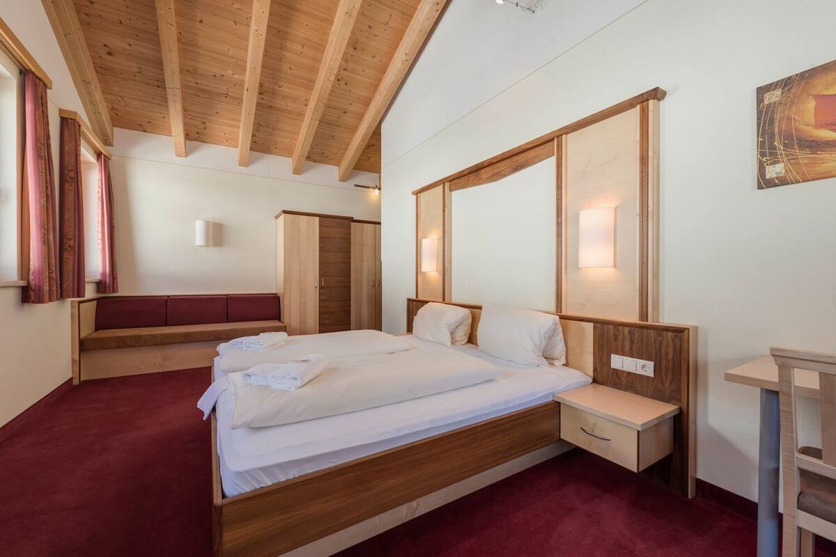 A bedroom with a wooden bed, a bedside table, a bench, and a wardrobe.