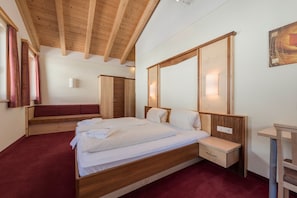 A bedroom with a wooden bed, a bedside table, a bench, and a wardrobe. - Hotel Abendrot by Alpeffect Hotels (Ischgl)
