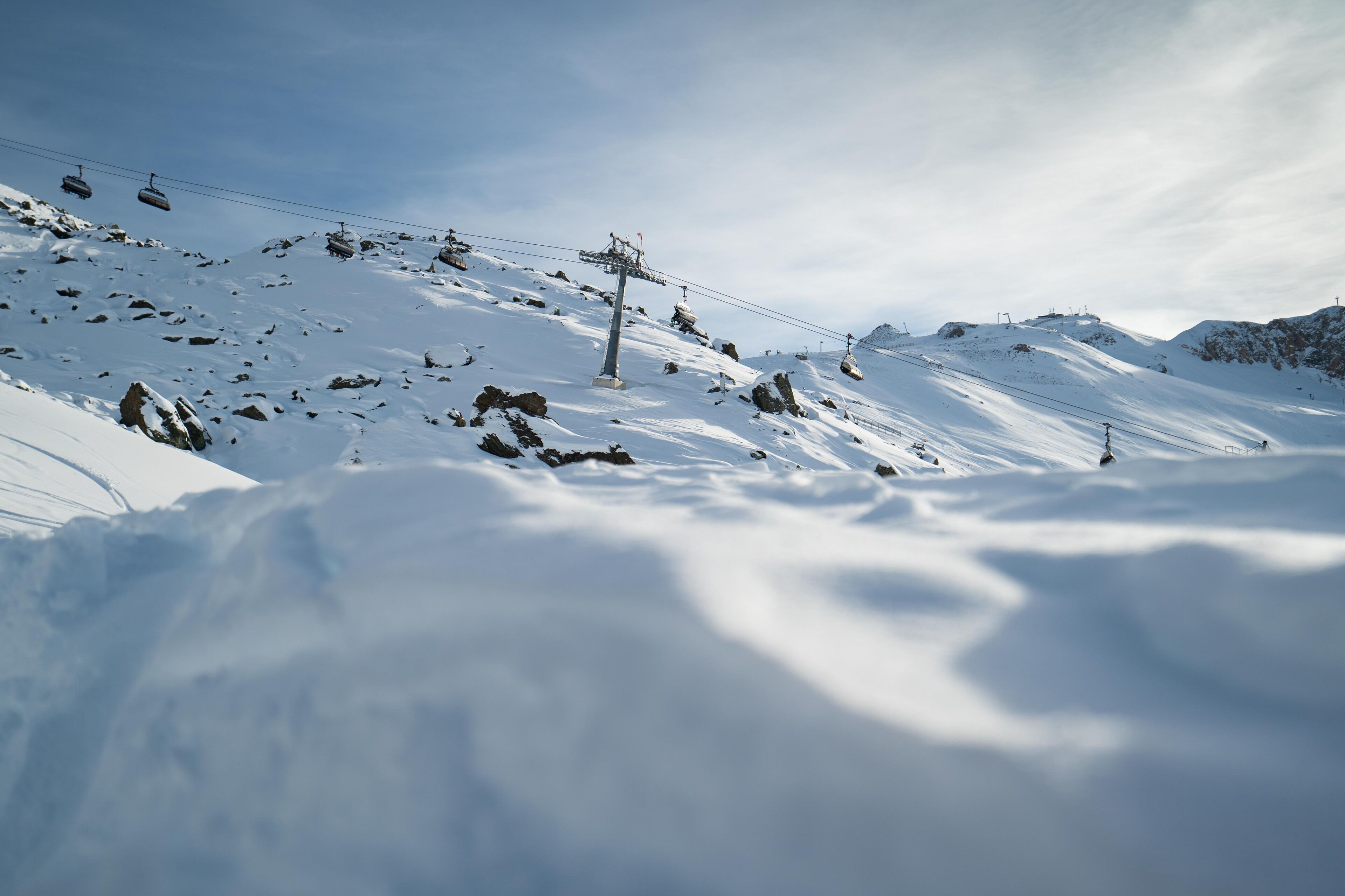 Pendiente nevada de una montaña con un telesilla y afloramientos rocosos.