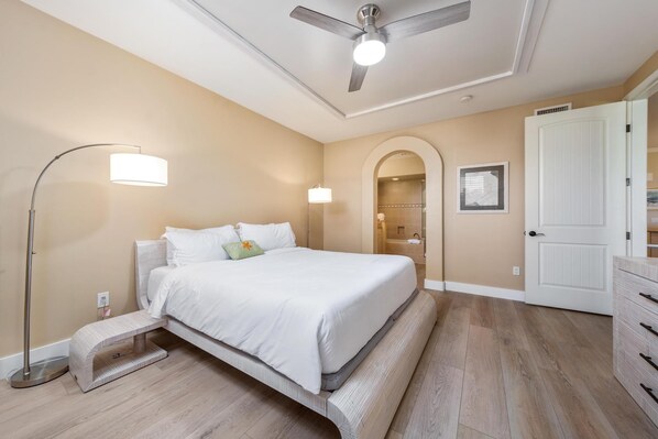 A bedroom with a bed, a standing lamp, a ceiling fan, and a door.