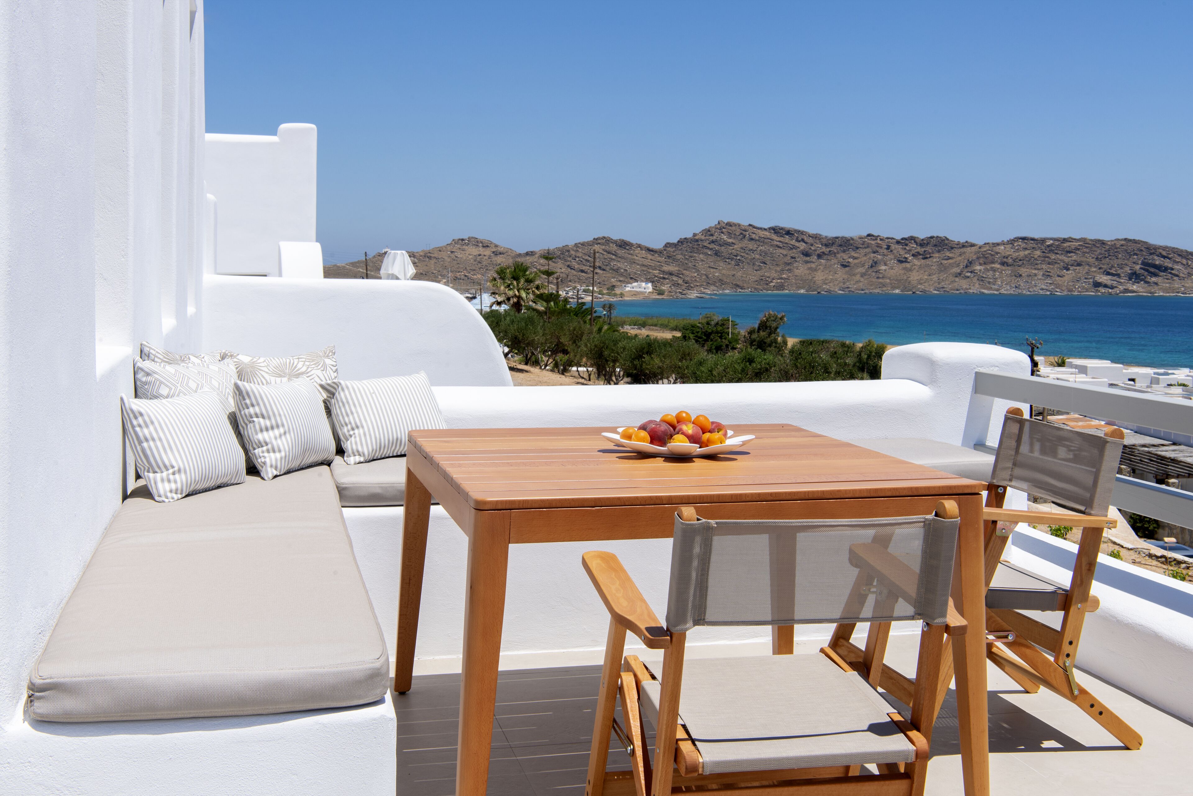 Eine Terrasse mit einem Holztisch, gepolsterten Sitzgelegenheiten und einer Obstschale.