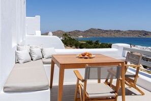 A terrace with a wooden table, cushioned seating, and a bowl of fruit. - Kymo Luxury Suites Paros (Paros)