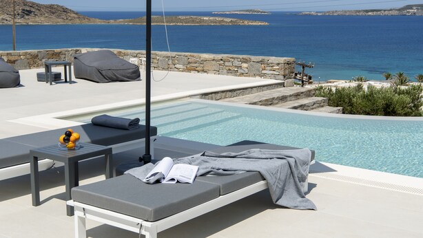 A poolside area with lounge chairs, a small table, and a book. - Kymo Luxury Suites Paros (Paros)