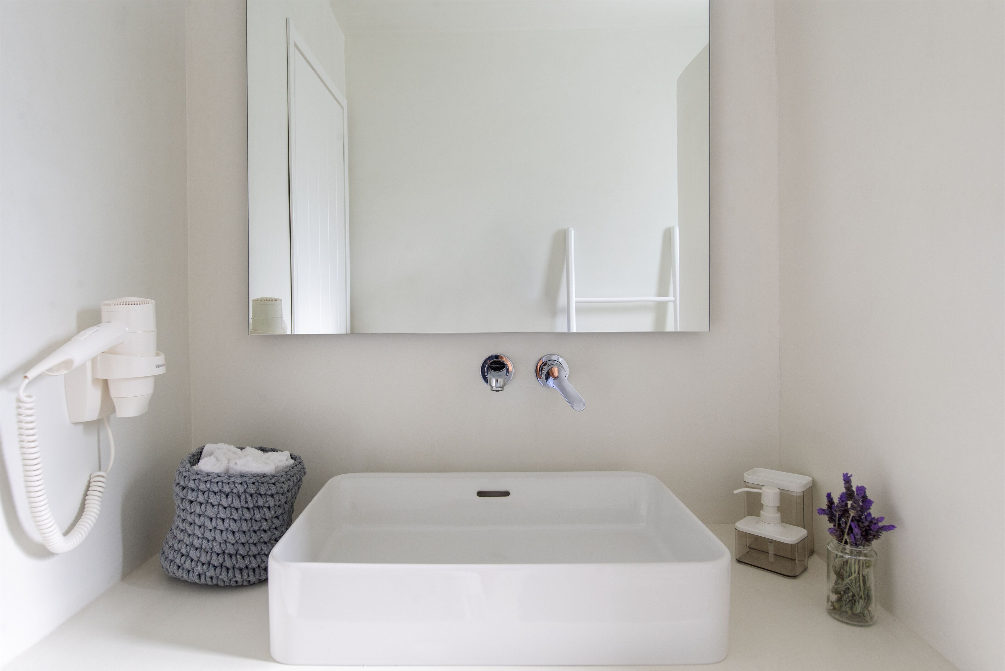 Un baño con lavamanos blanco, un espejo, dispensador de toallas y un cubo de basura.
