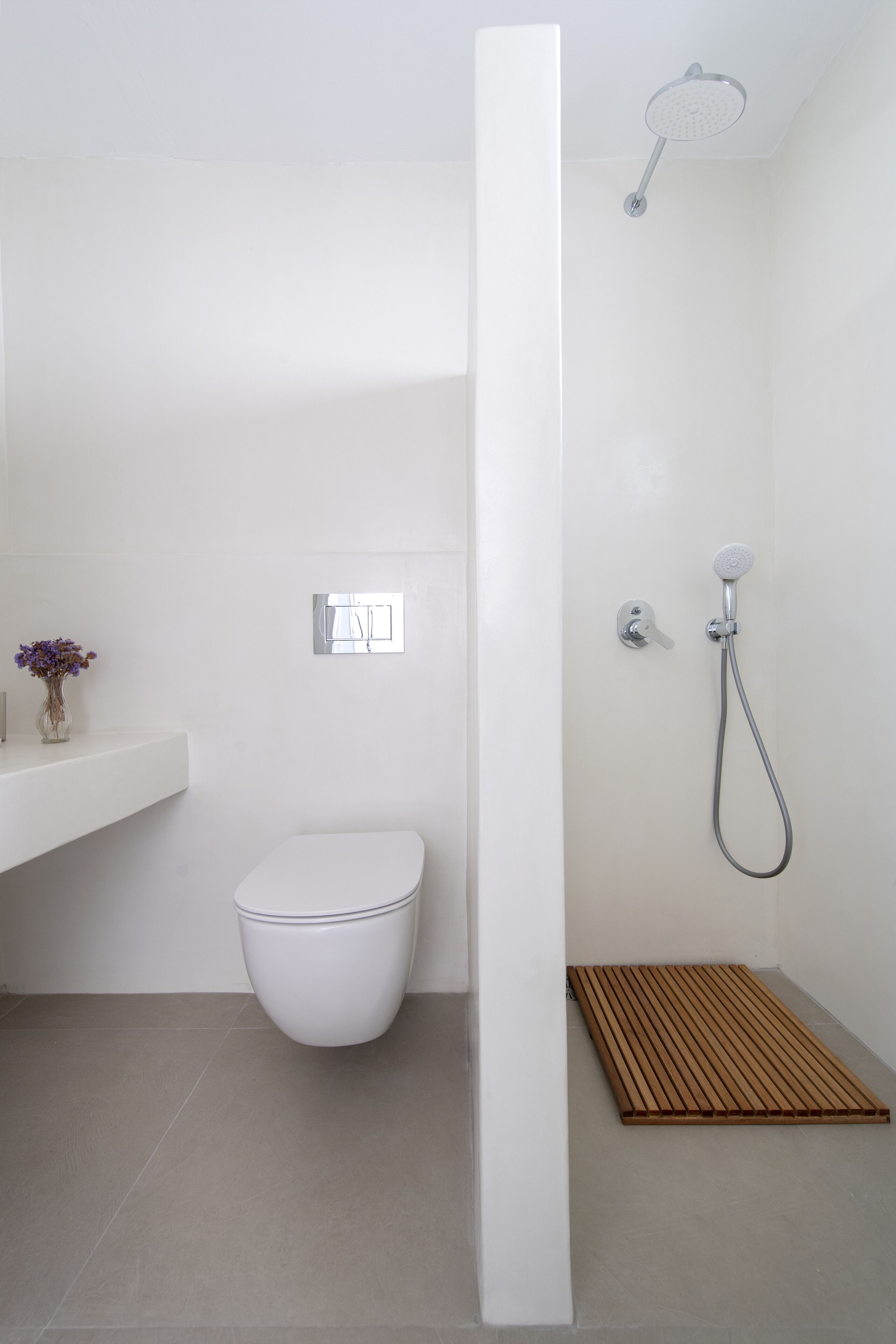 Et moderne badeværelse med toilet, brusebad og en lille træmåtte.
