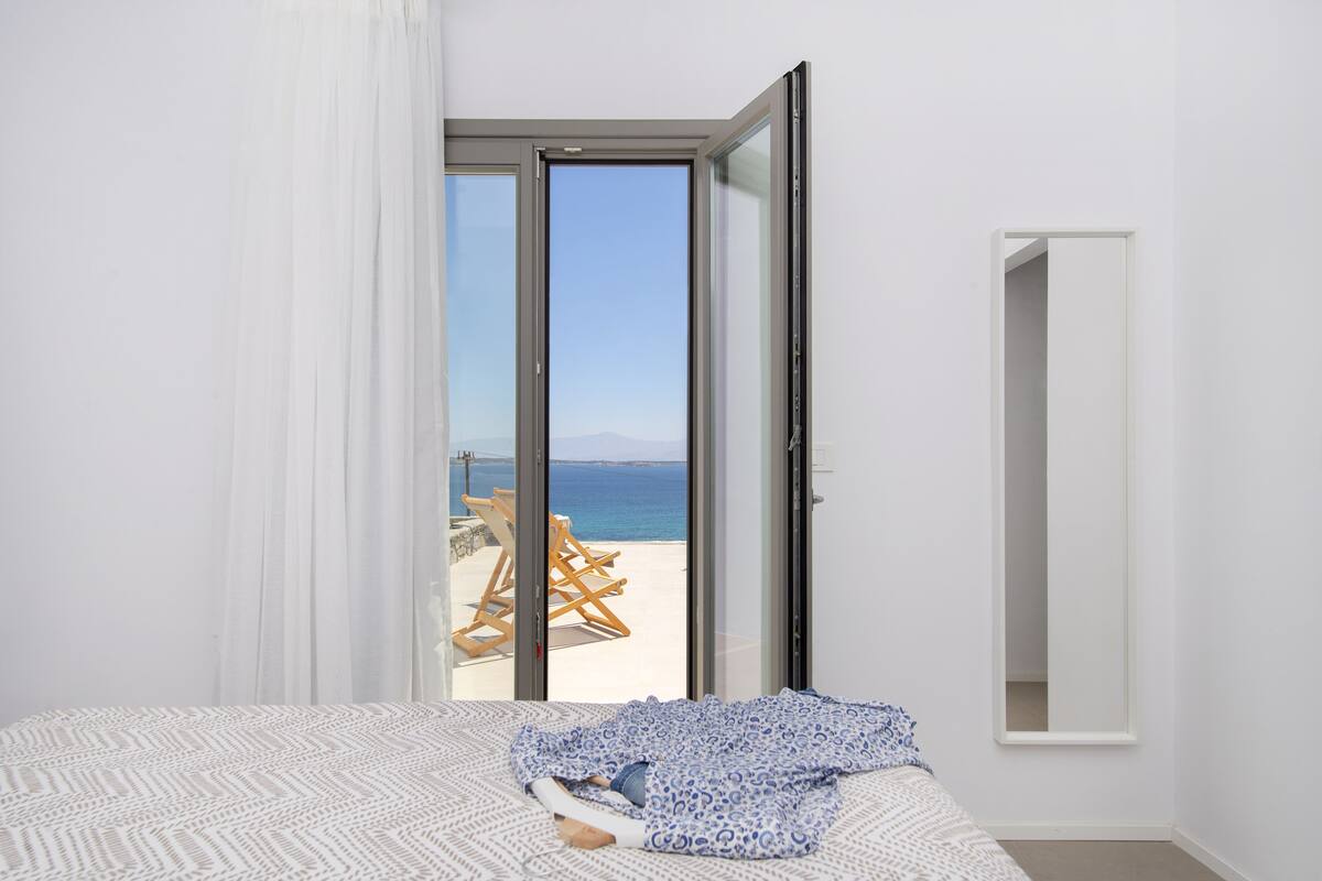 A bedroom with a bed, a large window, and a view of the beach.