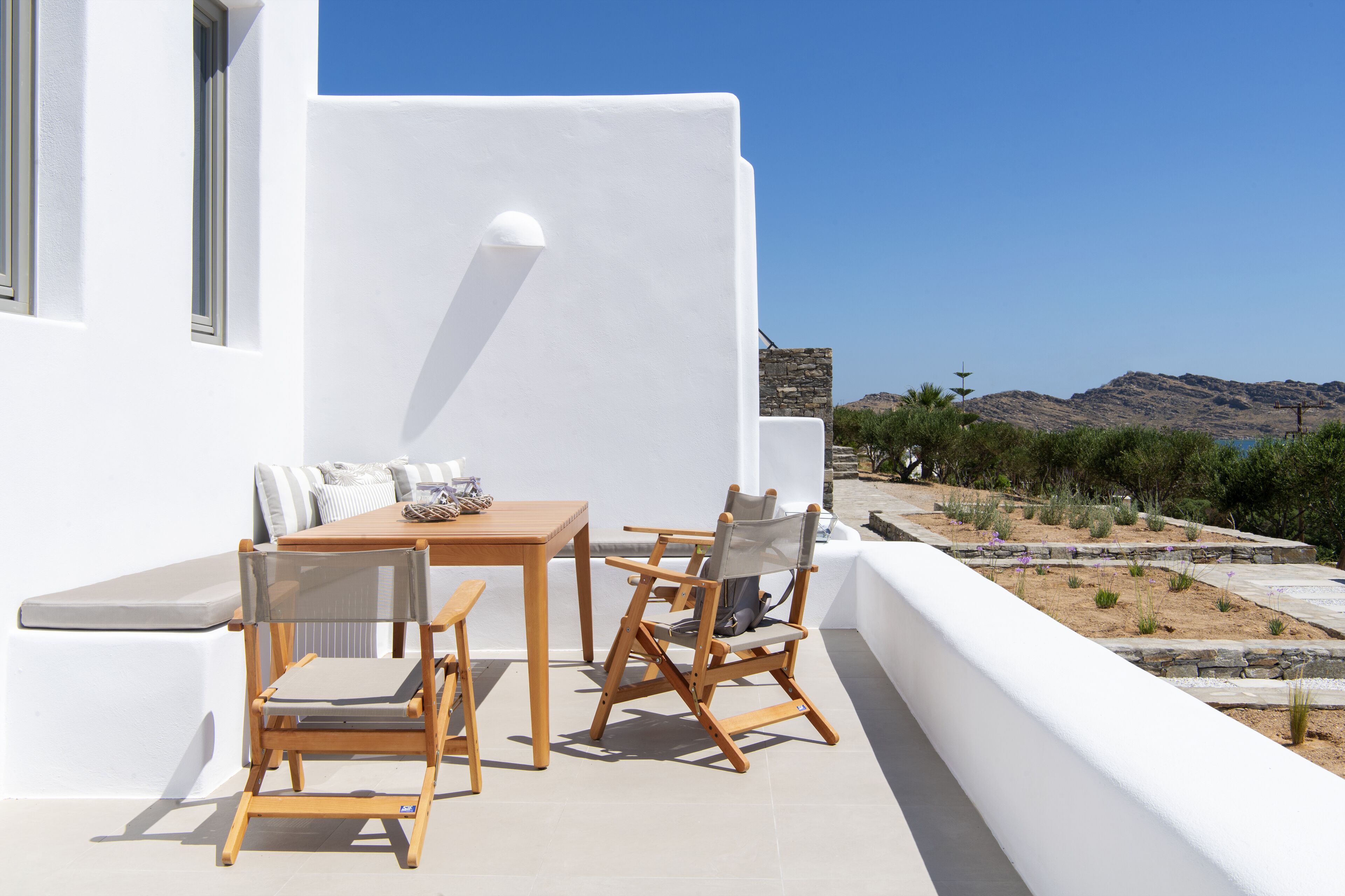 Un espace extérieur aménagé avec une table et des chaises en bois, un banc rembourré et une vue sur un paysage montagneux.