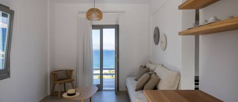A minimalist living room with a wooden table, a sofa, and a view of the sea through a glass door.
