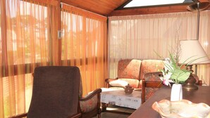 A cozy room with a wooden ceiling, a sofa, a chair, a table with a lamp, and a vase with flowers.