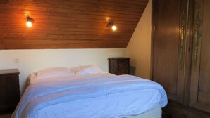 A bedroom with a wooden ceiling, a bed with white bedding, a nightstand, and a wooden wardrobe.