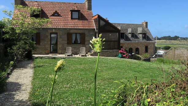A stone house with a sloped roof, a gravel path, and a grassy lawn.