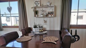 A dining area with a wooden table, brown leather chairs, a decorative shelf with items, and a view through the window. - Watten-Blick-Huisje -view of the Wadden Sea (UNESCO World Heritage Site) (Westerland)