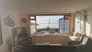 A living room with a large window, a television, a sofa, and a coffee table. - Watten-Blick-Huisje -view of the Wadden Sea (UNESCO World Heritage Site) (Westerland)