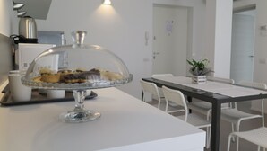 Cozinha moderna com eletrodomésticos brancos, uma vitrine de vidro com doces e um espaço de jantar com cadeiras e mesa brancas.