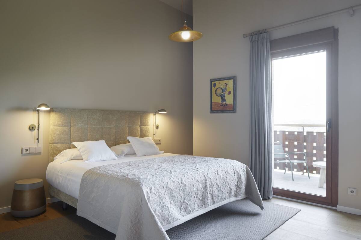 Ein Schlafzimmer mit einem großen Bett, einem Nachttisch, einer Lampe und Blick auf den Balkon.