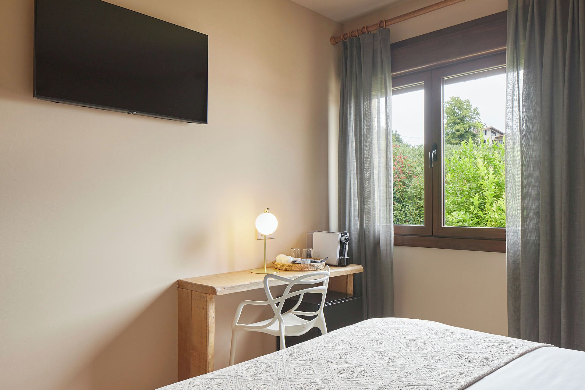 A bedroom with a bed, a desk with a lamp, and a window with curtains.