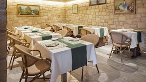 A dining area with stone walls, multiple tables set with white tablecloths and green runners, wicker chairs, and framed artwork on the walls. - Olivi1948 - Boutique Guesthouse (Usurbil)