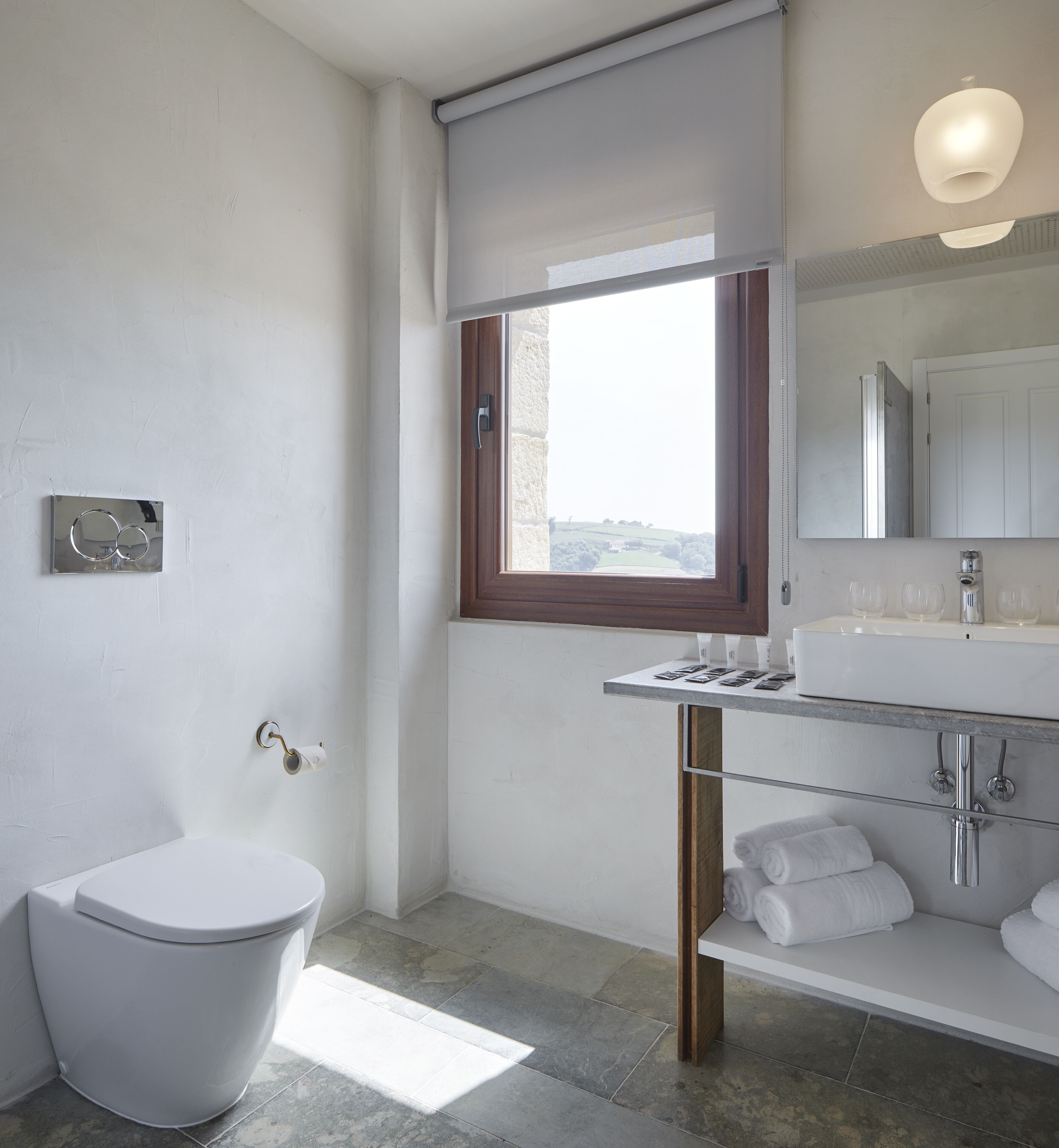 A modern bathroom with a toilet, a sink with a mirror, and a window.