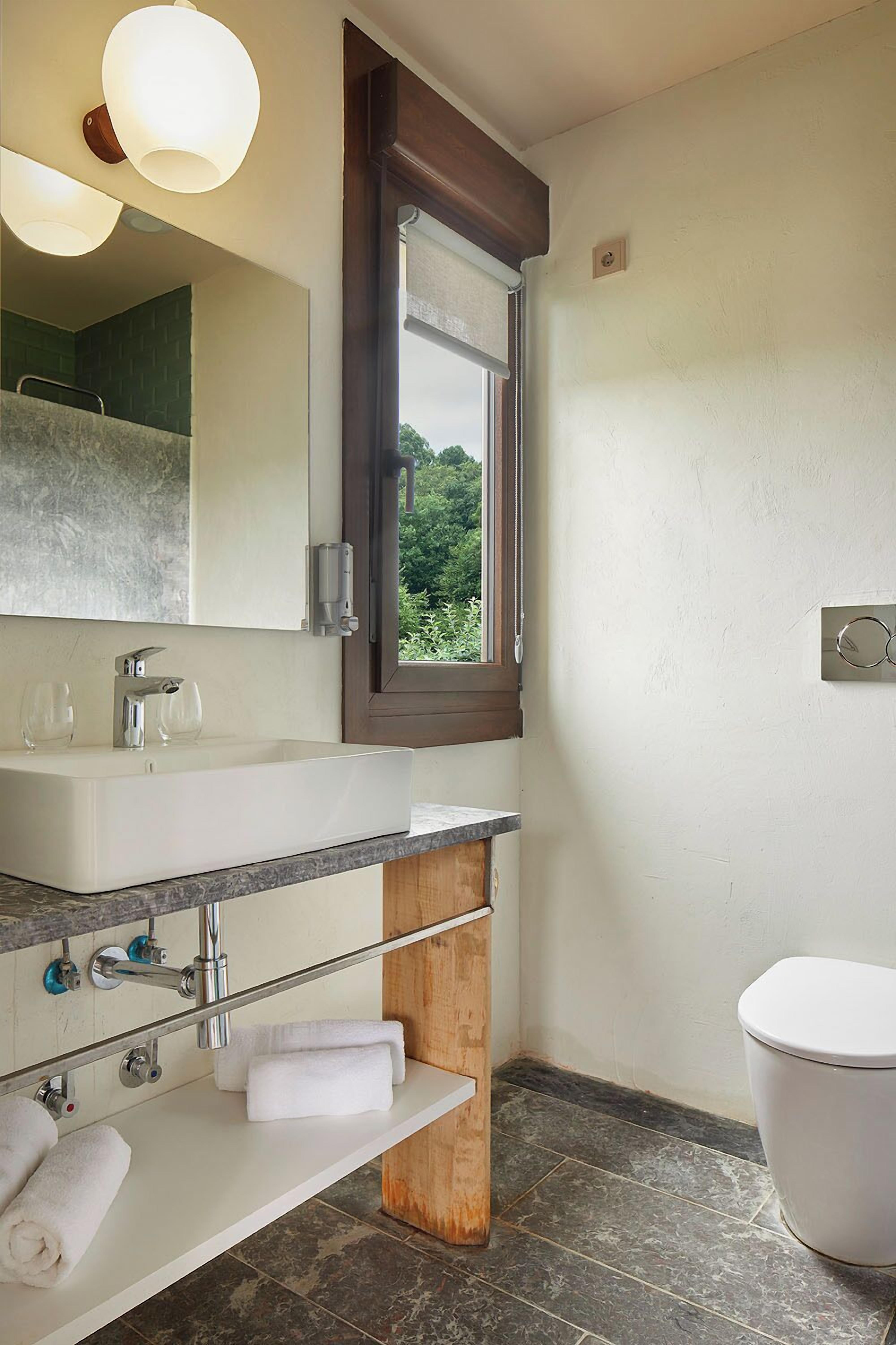 A bathroom with a large mirror, a sink, a window, and a toilet.