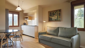A living room with a sofa, a dining table with chairs, a kitchen area, and a painting on the wall. - Olivi1948 - Boutique Guesthouse (Usurbil)
