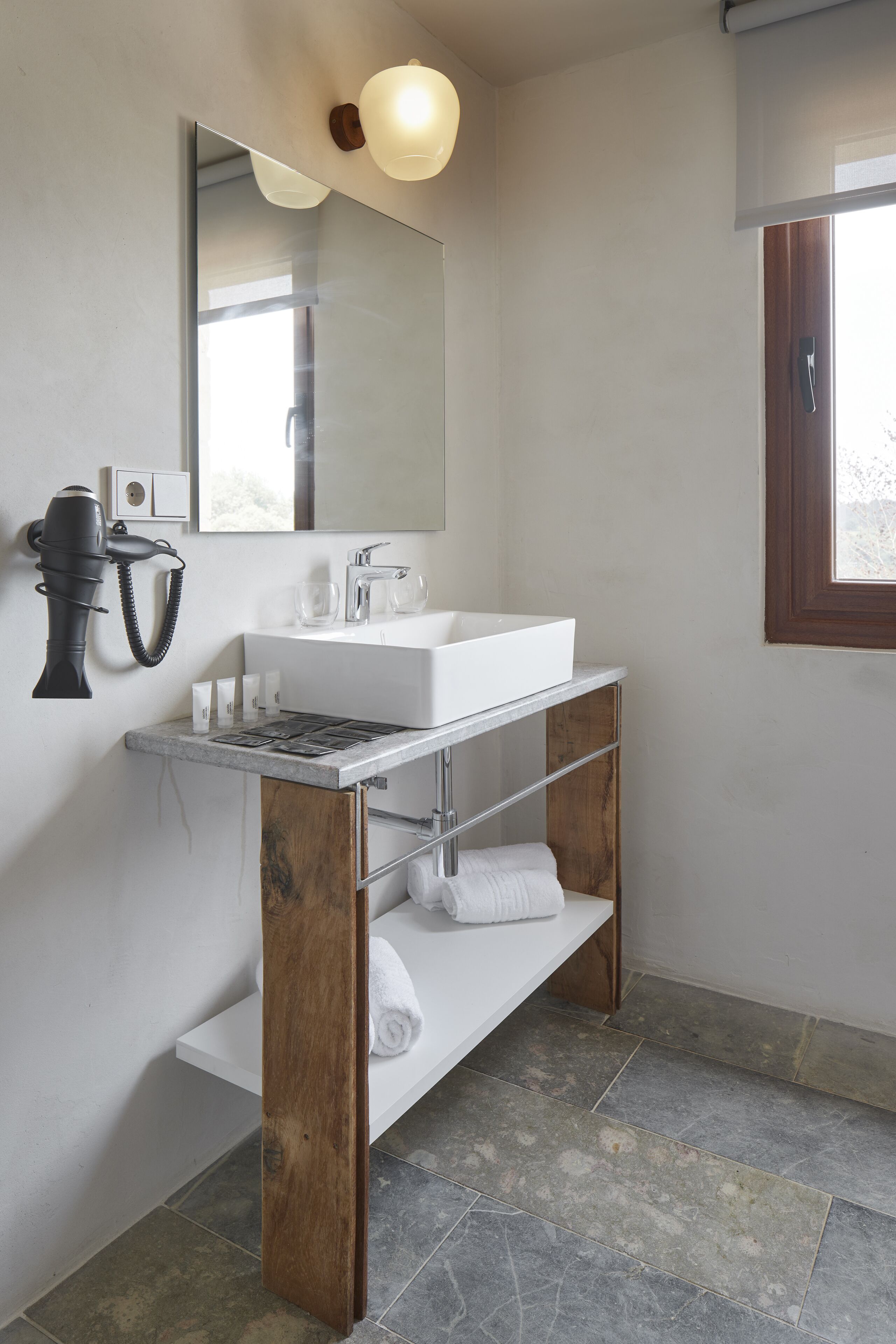 A bathroom with a white sink, a mirror, a hairdryer, and a window.
