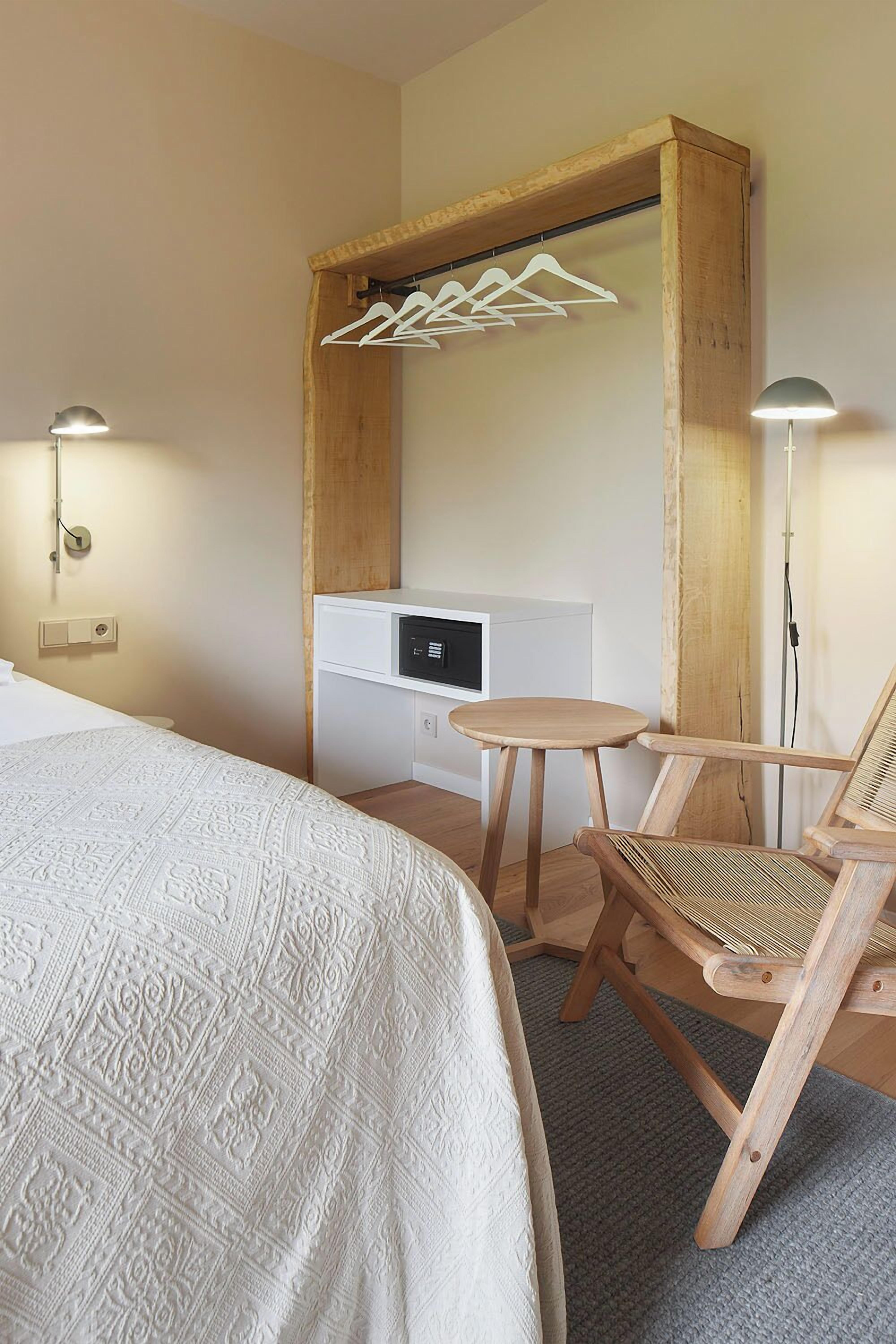 A bedroom with a bed, a wooden chair, a small table, and a wall-mounted heater.