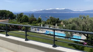Ein Balkon mit Blick auf einen Swimmingpool, eine gebirgige Landschaft und das Meer.