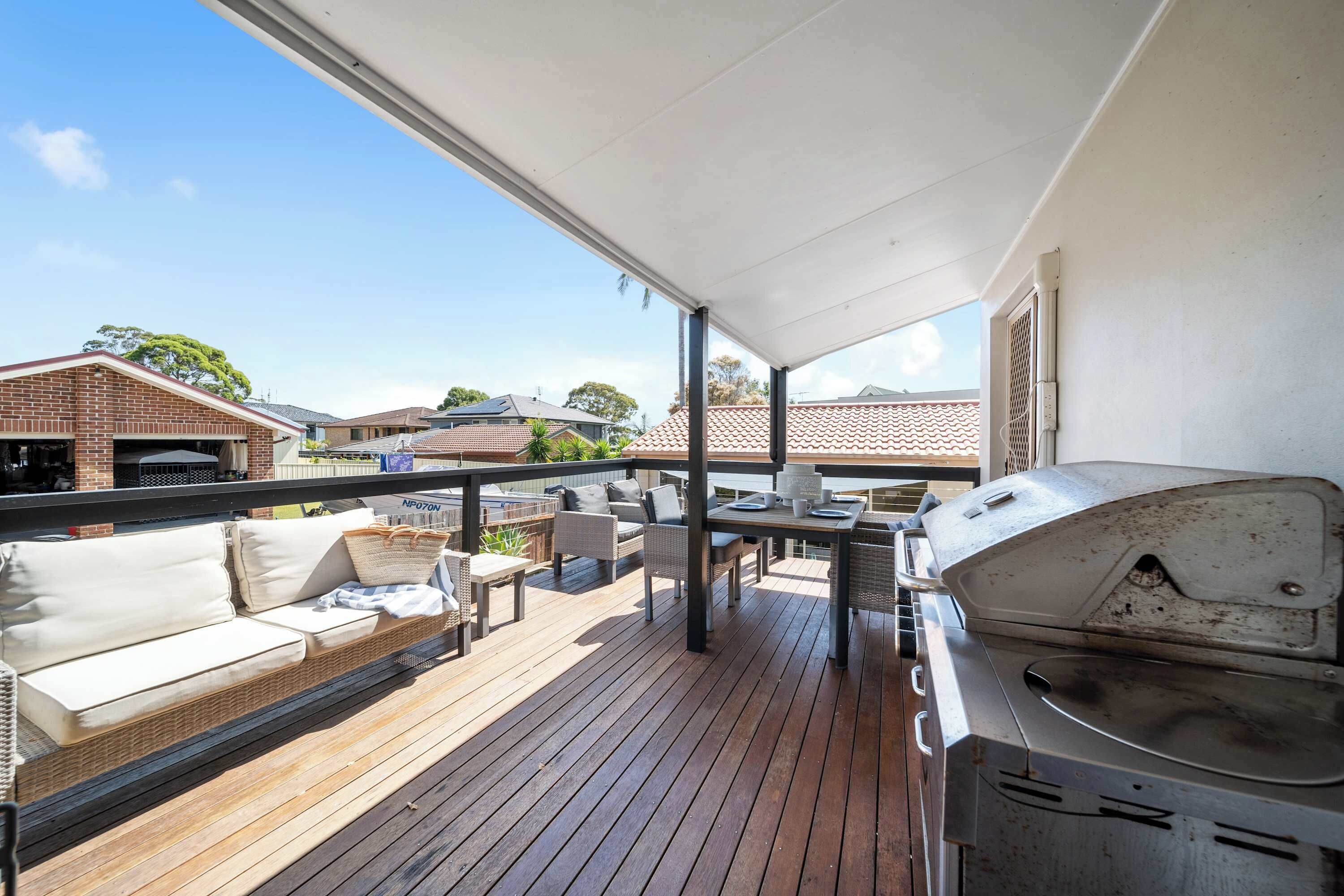 A covered outdoor deck with a grill, seating area, and a view of neighboring houses.