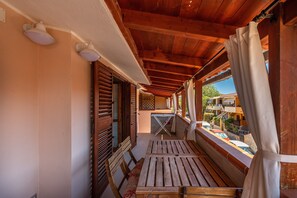 Un balcón de madera con una mesa y sillas, vista al exterior y una pequeña zona de estar al aire libre.