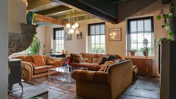 A cozy living room with a fireplace, a sofa, a coffee table, and large windows.