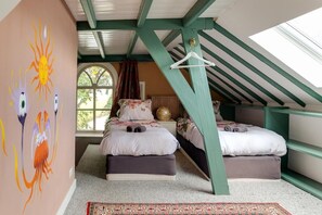 Un dormitorio con techo inclinado, dos camas, un ventanal grande y una pared con arte abstracto.
