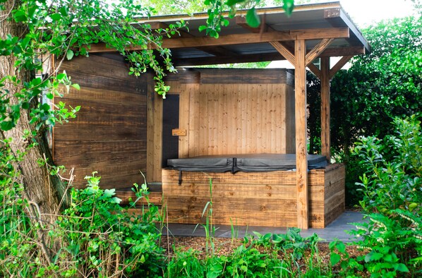 A wooden outdoor seating area with a bench and a wooden structure, surrounded by greenery. - BoHo Farmhouse – characterful farmhouse for up to 14 guests, sauna & jacuzzi (Kockengen)