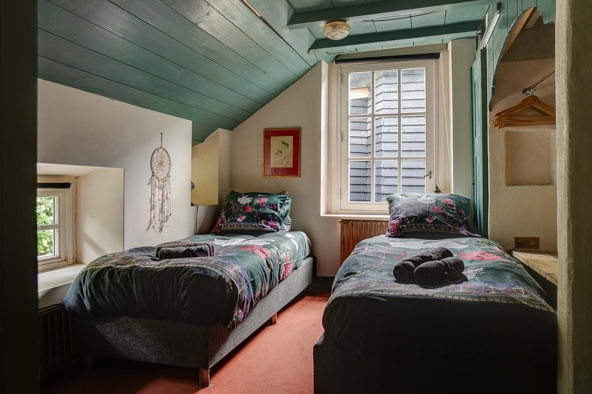 Ein Schlafzimmer mit zwei Betten, einem Fenster mit Rollläden, einem Traumfänger und einem gerahmten Bild an der Wand.