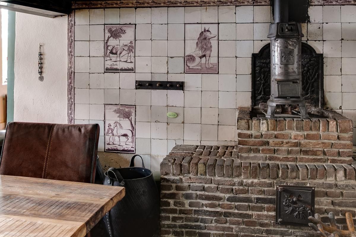 A rustic interior with a brick fireplace, a tiled wall with animal illustrations, and a leather chair.