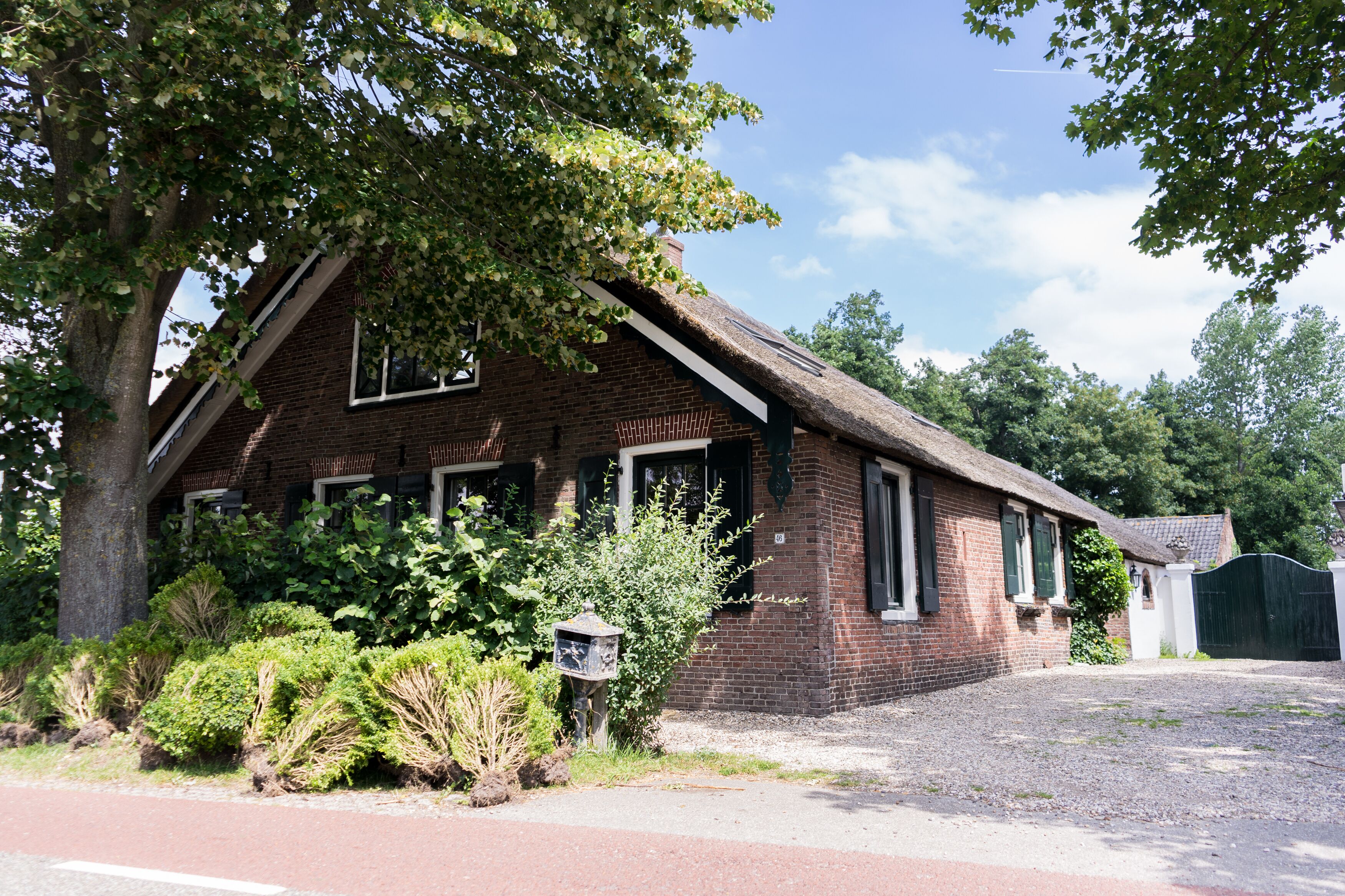 A brick building with a sloped roof, surrounded by greenery and a gravel driveway.