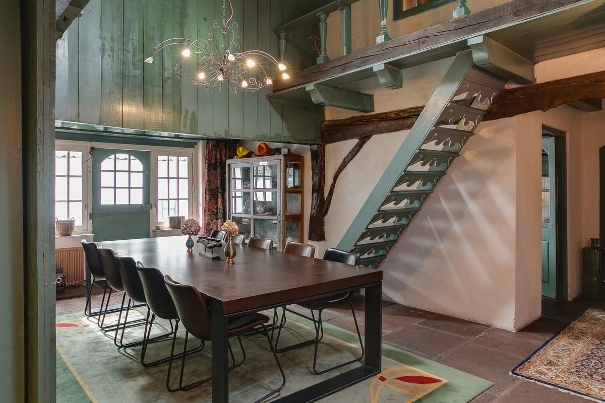 Een eetruimte met een houten tafel en stoelen, een kroonluchter en een trap.