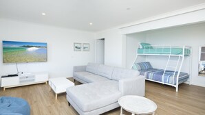 A modern living room with a grey sofa, a white coffee table, a bunk bed with blue bedding, a flat-screen TV on the wall, and a wooden floor. - Aqua Palm with Sweeping Views of On Mile (Forster)