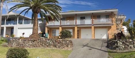 A two-story building with a balcony, a stone wall, and a palm tree.