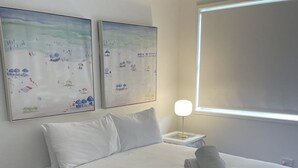 A neatly made bed with white linens, a gray headboard, and a white pillow. There are two wall-mounted paintings depicting a winter scene. A bedside table with a lamp is visible. - Aqua Palm with Sweeping Views of On Mile (Forster)