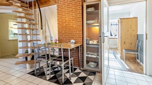 Una stanza con parete in mattoni, una scala in legno, un tavolo da pranzo con sedie, una vetrina e una porta in legno che dà su un'altra stanza.