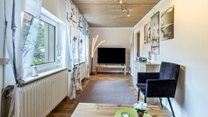 Un soggiorno moderno con televisore, divano, tavolino e finestra con tende.