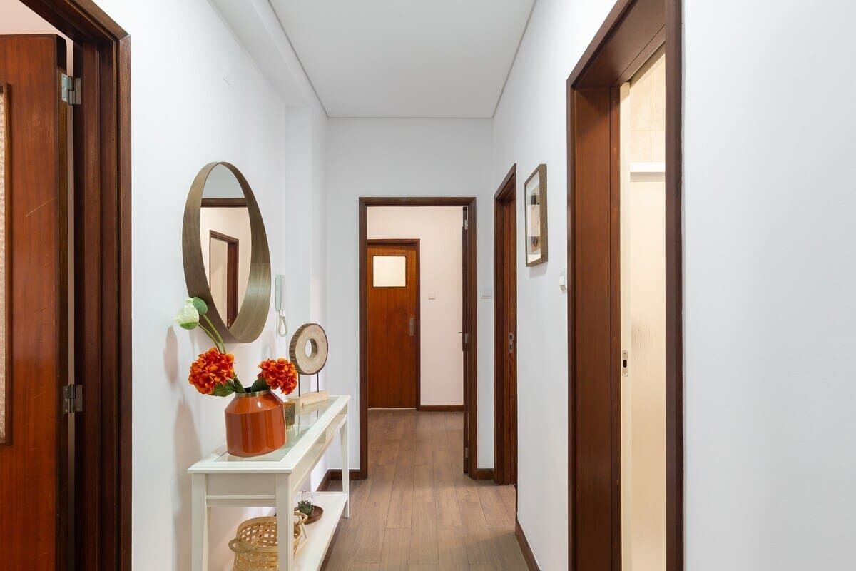 A hallway with wooden doors, a white console table with a mirror, and a vase with flowers.