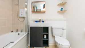 A modern bathroom with a bathtub, toilet, and a vanity with a mirror and shelves. - Stylish 2 Bedroom Apartment Aberdeen City Centre (Aberdeen)