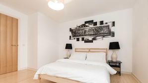 A bedroom with a wooden bed, white bedding, two bedside tables with lamps, and a wall-mounted abstract art piece. - Stylish 2 Bedroom Apartment Aberdeen City Centre (Aberdeen)