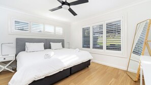 A bedroom with a bed, a bedside table, a ceiling fan, and large windows with blinds. - Amaroo - Uninterrupted 180 degree water views (Gerroa)